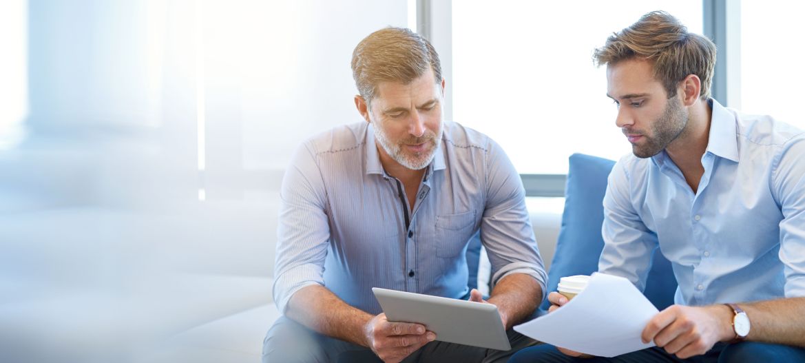 Mature businessman using a digital tablet to discuss information with a younger colleague in a modern business lounge