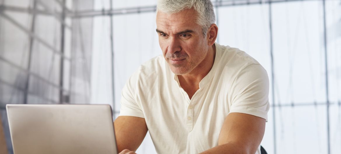 Portrait of young caucasian businessman in casual shirt using laptop computer at workplace