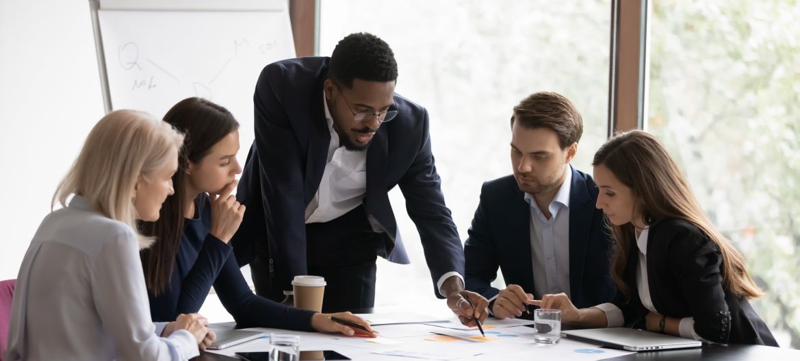 Confident african American male boss work cooperate with diverse team at office briefing, focused biracial businessman head meeting, collaborate discuss business ideas with colleagues at meeting