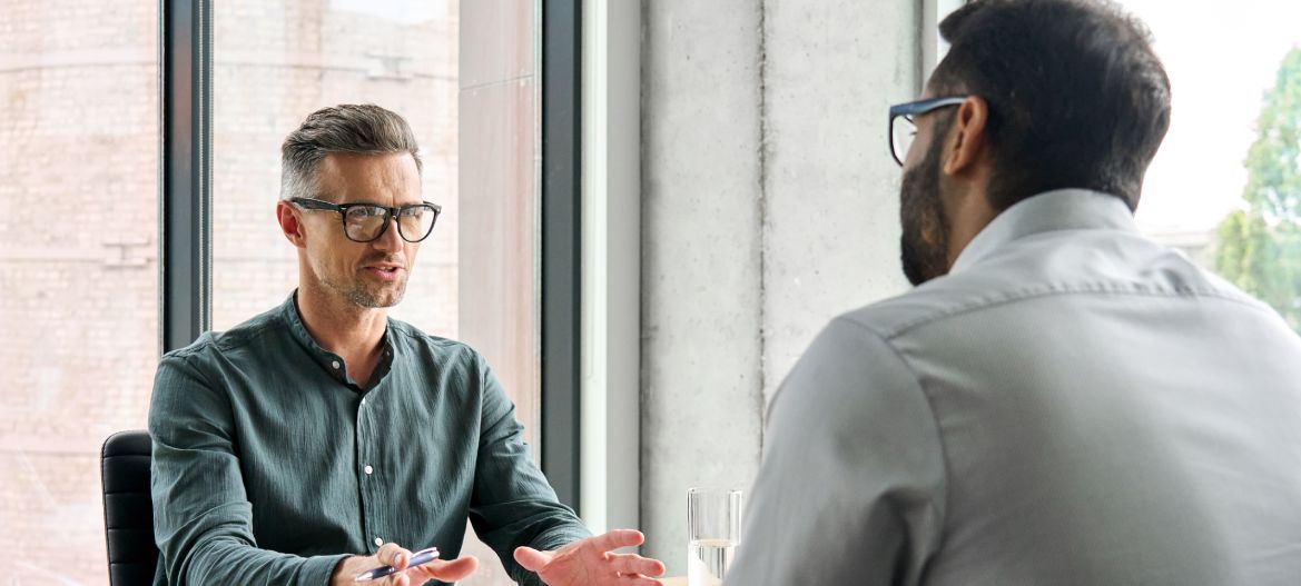 Two diverse business executive partners negotiating at board meeting, manager adviser consulting client discussing financial partnership contract sitting at table in office. Job interview concept.